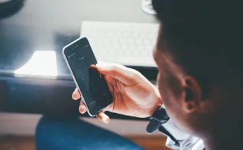 A man seated at a desk, engaged with his phone, exploring methods to unlock Samsung phone without password.