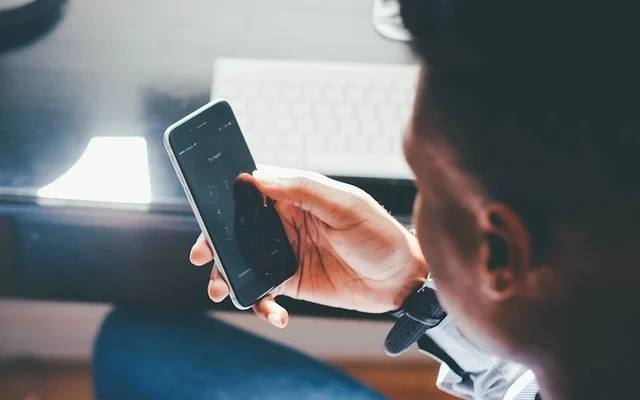 A man seated at a desk, engaged with his phone, exploring methods to unlock Samsung phone without password.