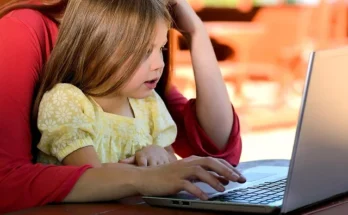 A woman and a child are focused on a laptop, sharing a learning experience together. Visit statekaidz.com for more.