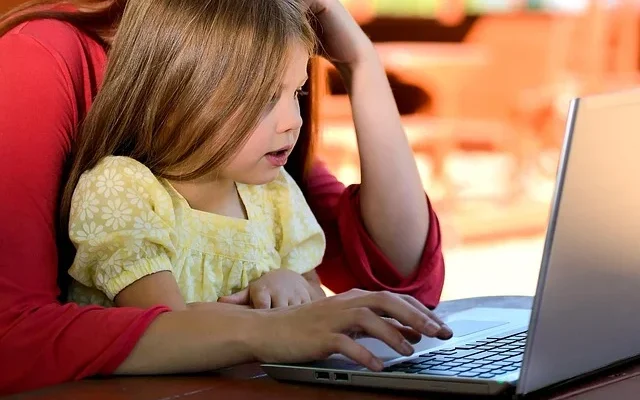 A woman and a child are focused on a laptop, sharing a learning experience together. Visit statekaidz.com for more.
