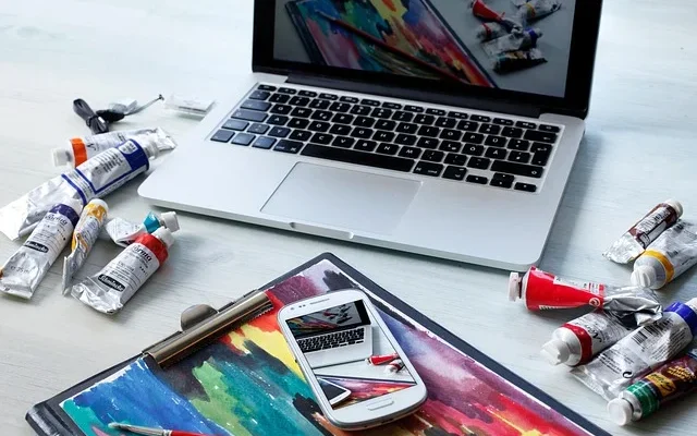 A table displays a laptop wizzydigital .org, paint brushes, and a smartphone, representing a blend of technology and artistry.